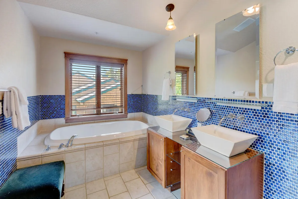 A spa-inspired bathroom featuring a luxurious bathtub, sleek washbasin, mosaic tile accents, and a window with adjustable blinds. The space is designed for relaxation and rejuvenation after a day of adventure.
