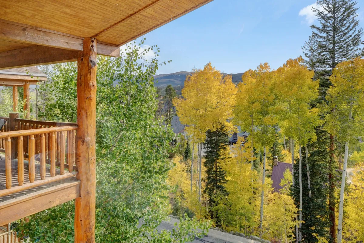A tranquil balcony scene overlooking vibrant yellow trees set against a mountain backdrop. The wooden railing suggests a cozy vantage point for enjoying nature, morning coffee, or the changing seasons.