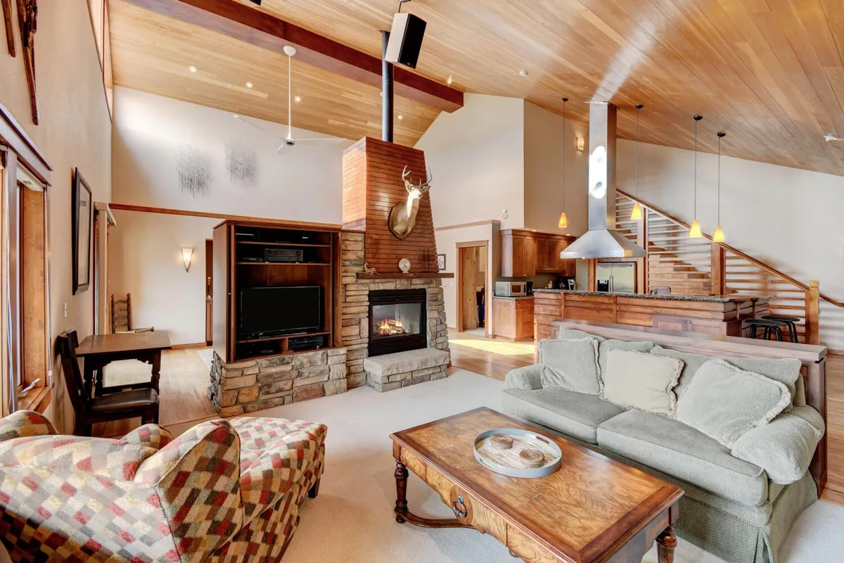 This image showcases the main great room with a plush sofa centered around a gas fireplace, complemented by a modern wooden staircase and expansive windows that flood the space with natural light. The room exudes warmth, inviting relaxation and group gatherings, and hints at an open-concept layout that encourages conversation and shared experiences.