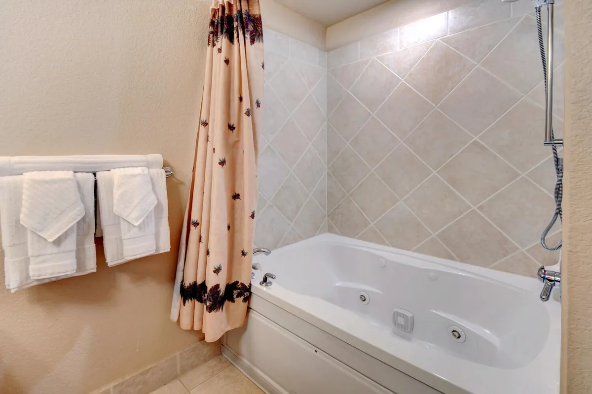 A tranquil bathroom with a large jacuzzi tub, decorative shower curtain, and neatly arranged towels. The space exudes relaxation, inviting guests to unwind after an active day.