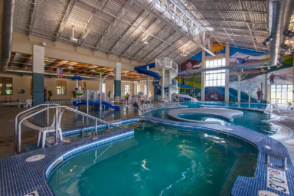A lively indoor pool area featuring twisting water slides, a decorative mural, and children happily playing in the water. The scene captures a joyful, energetic environment ideal for families seeking fun and recreation.