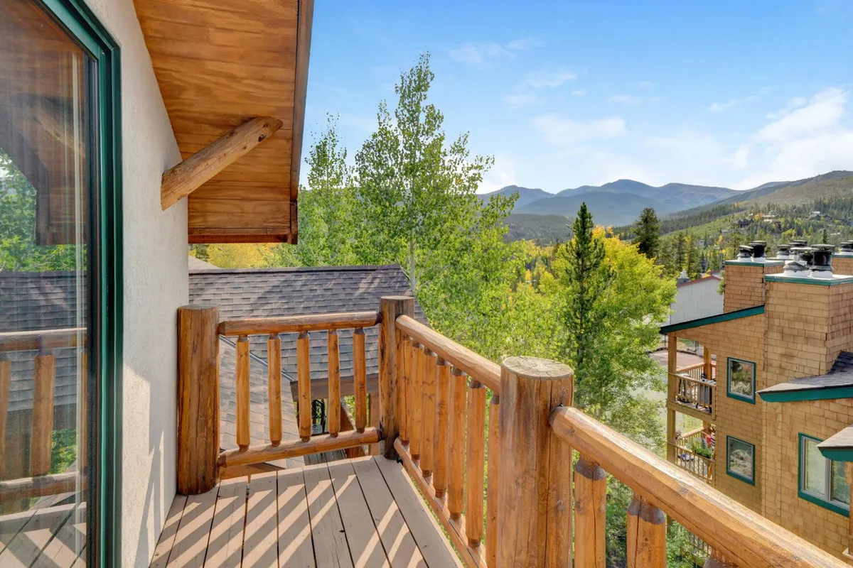 A serene exterior view from a wooden railing, overlooking lush greenery and distant mountains. The perspective suggests a peaceful retreat, ideal for enjoying morning coffee, quiet reading, or birdwatching, with vibrant seasonal colors adding to the appeal.