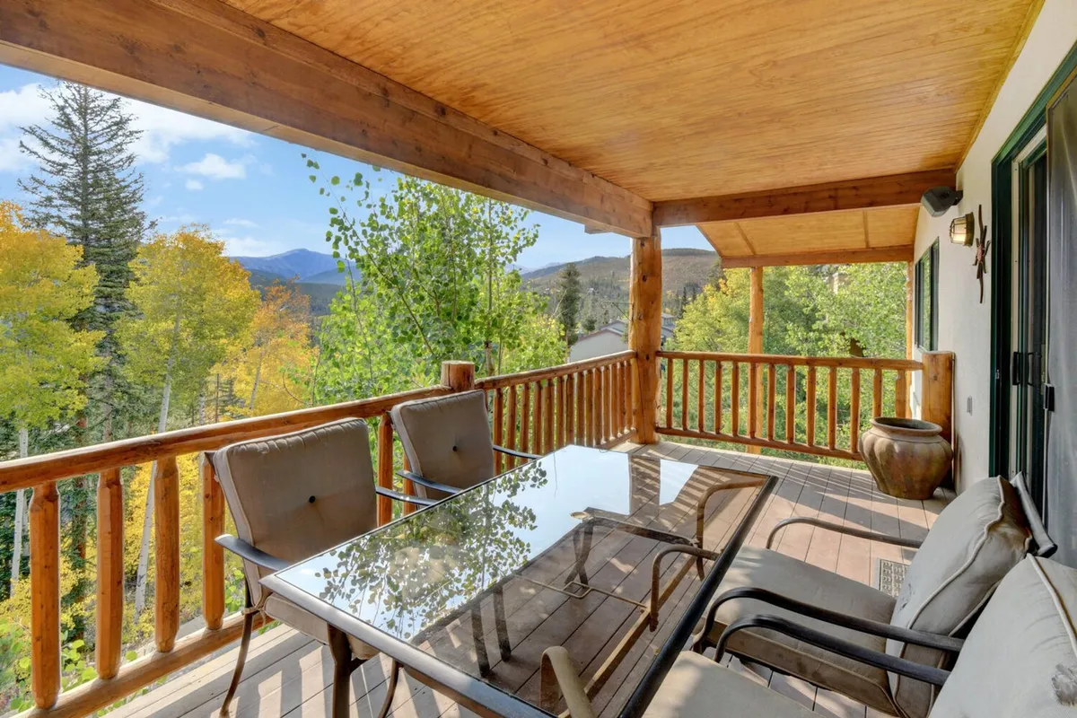 This exterior deck scene features a glass dining table, comfortable seating, and a wooden balcony railing set amid lush trees. It evokes opportunities for sipping coffee, relaxing outdoors, or hosting evening barbecues while enjoying peaceful mountain views.