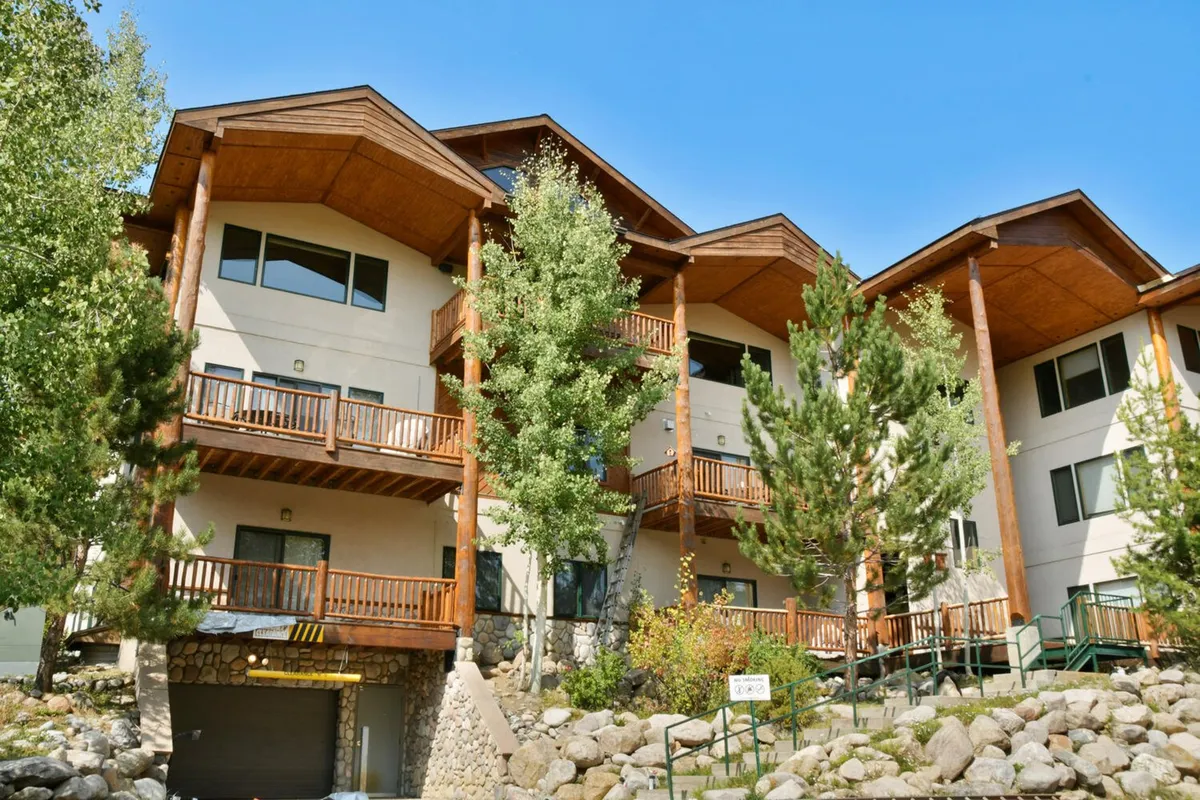 The exterior of the property features wooden balconies and a stone base, surrounded by green trees, conveying a welcoming and serene atmosphere. The design invites outdoor relaxation and gathering, with the option to watch sunsets or stargaze, all set against a beautiful natural backdrop.
