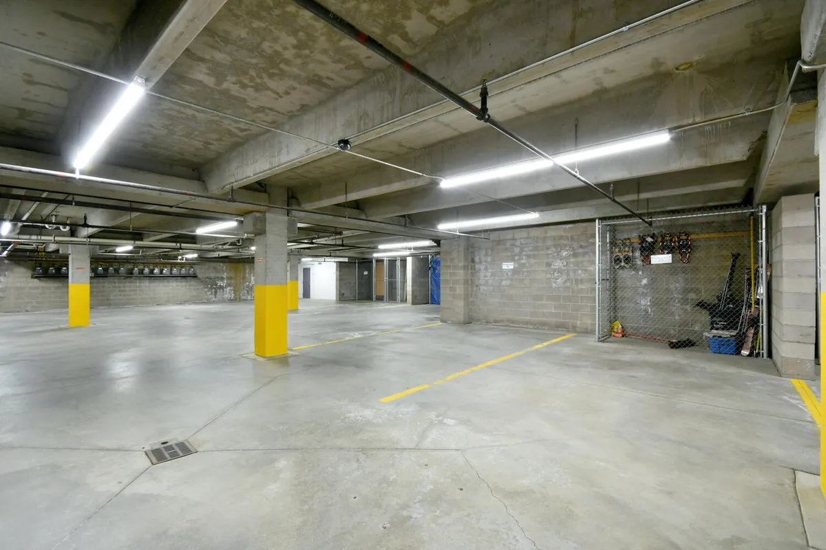 This image depicts a heated garage area defined by concrete pillars, yellow markings, and overhead lighting. The space is organized for easy vehicle parking and offers visible bicycle storage options, emphasizing practicality and accessibility.